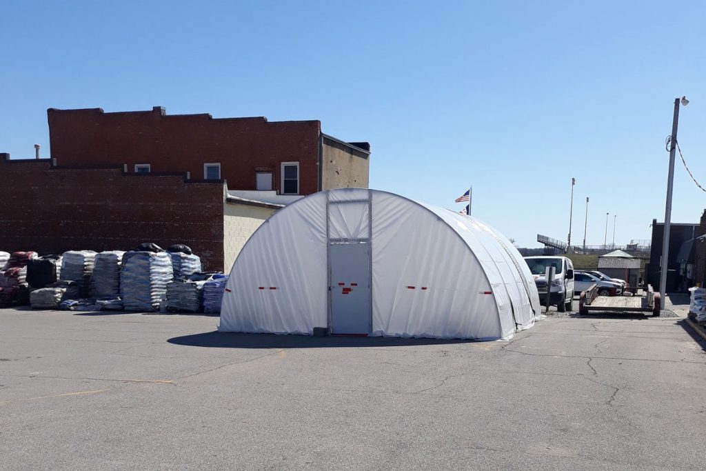 A white, dome-shaped tent is set up in the Carlisle Hardware parking lot with stacks of materials nearby. A truck is parked beside it, and buildings frame the background under a clear blue sky. Stop by our store to check out this seasonal event!